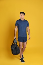 Handsome man with sports bag on yellow background