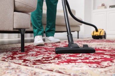 Photo of Dry cleaner's employee hoovering carpet with vacuum cleaner indoors, selective focus