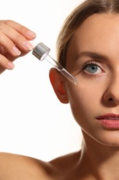 Woman applying cosmetic serum onto her face on white background, closeup