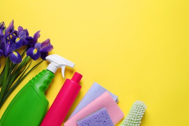 Spring cleaning. Detergents, flowers, sponge, brush and rags on yellow background, flat lay. Space for text