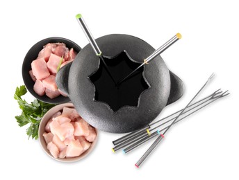 Fondue pot with oil, forks, raw meat pieces and parsley isolated on white, top view