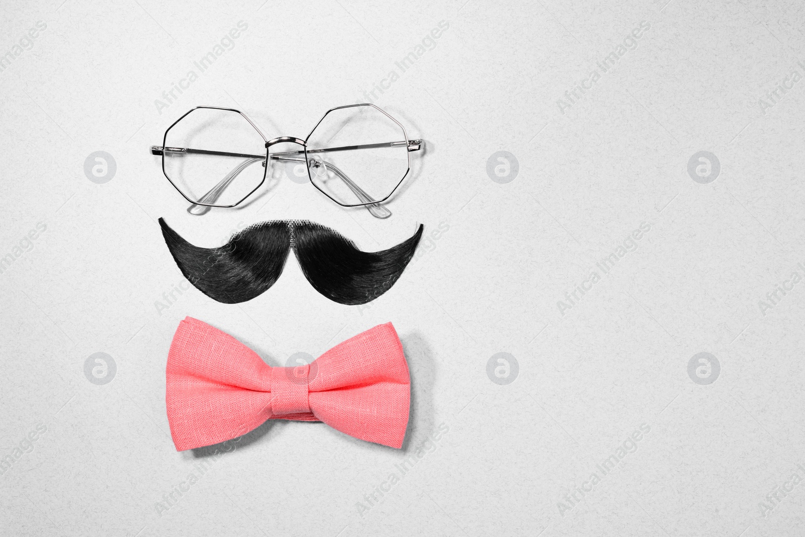 Photo of Man's face made of artificial mustache, bow tie and glasses on light grey background, top view. Space for text