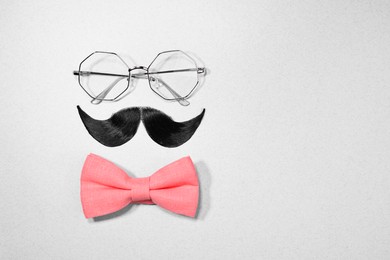 Photo of Man's face made of artificial mustache, bow tie and glasses on light grey background, top view. Space for text