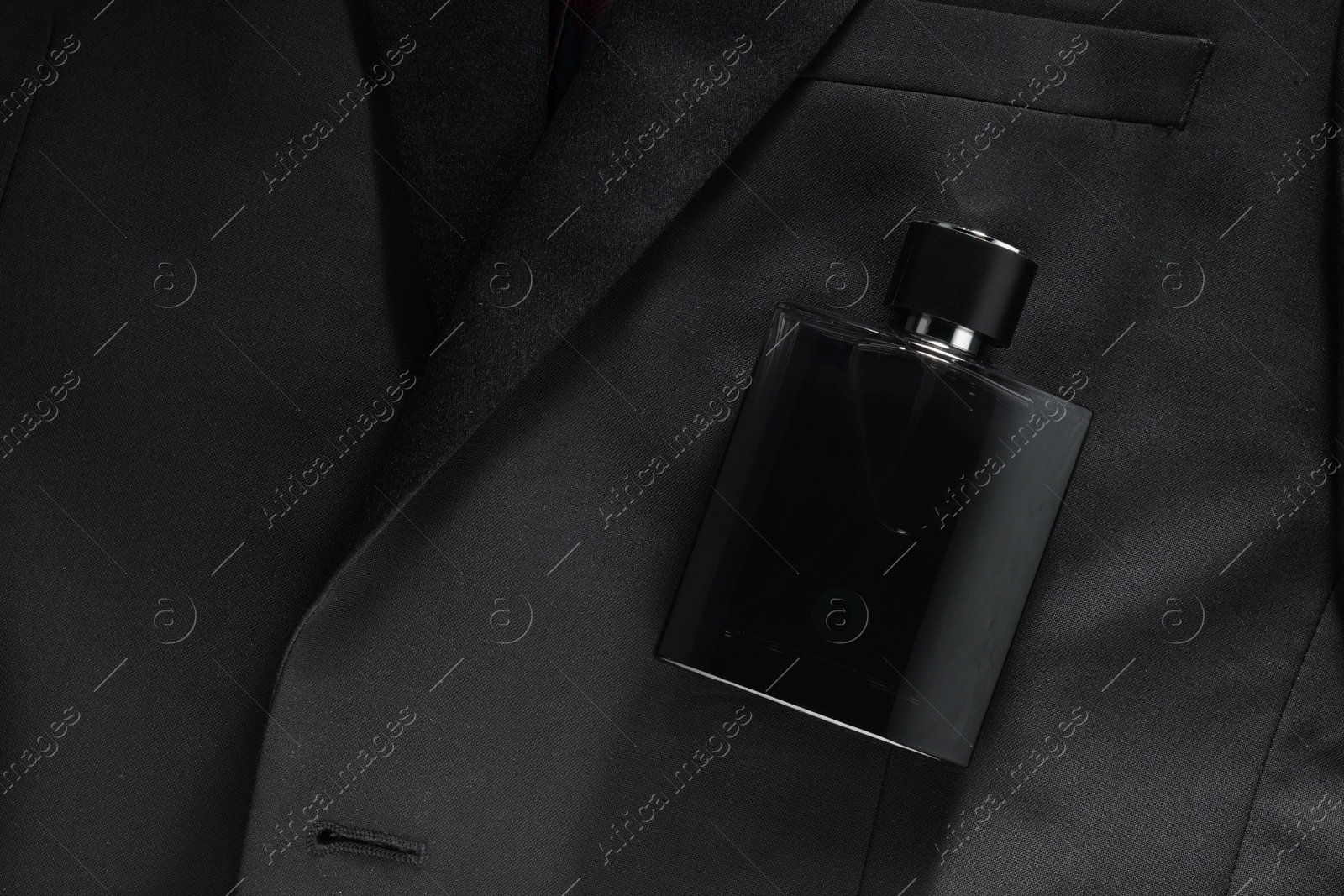 Photo of Luxury men's perfume in bottle on black jacket, top view. Space for text