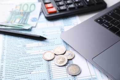 Tax forms, money, pen, calculator and laptop on table, closeup