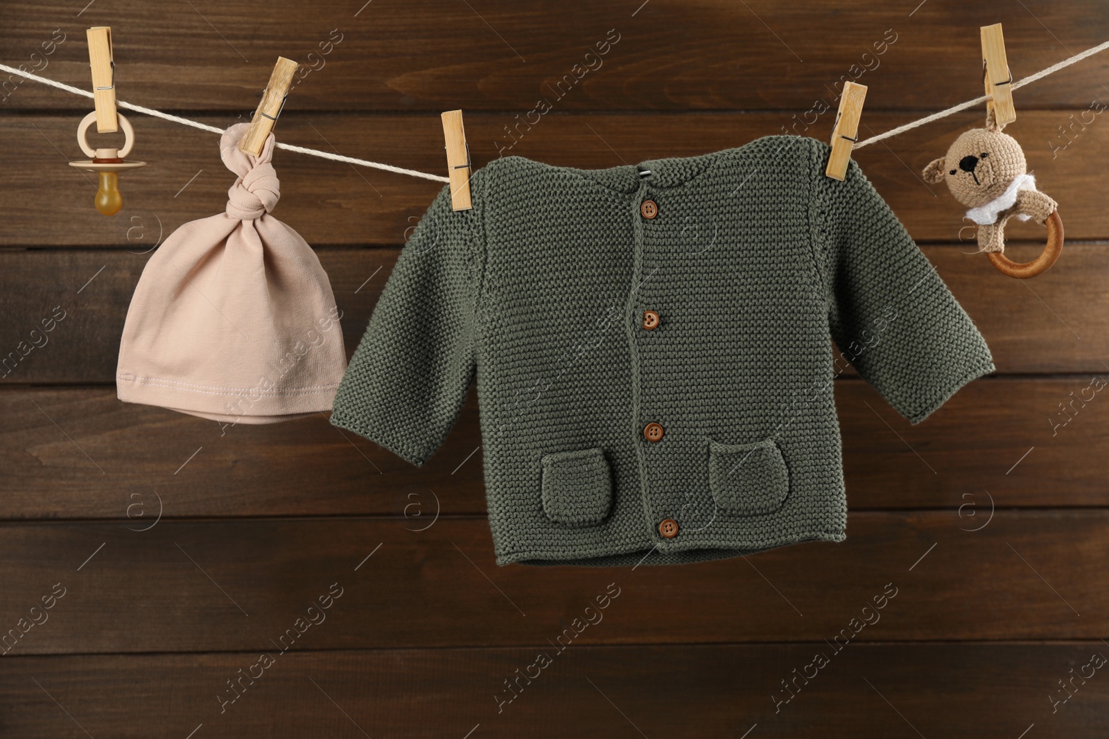 Photo of Baby clothes and accessories hanging on washing line near wooden wall