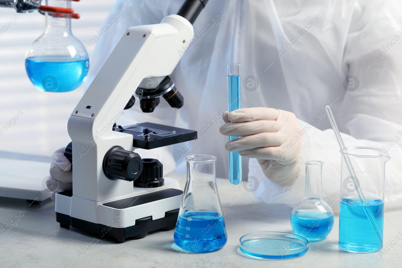 Photo of Scientist with test tube of light blue liquid near microscope in laboratory, closeup