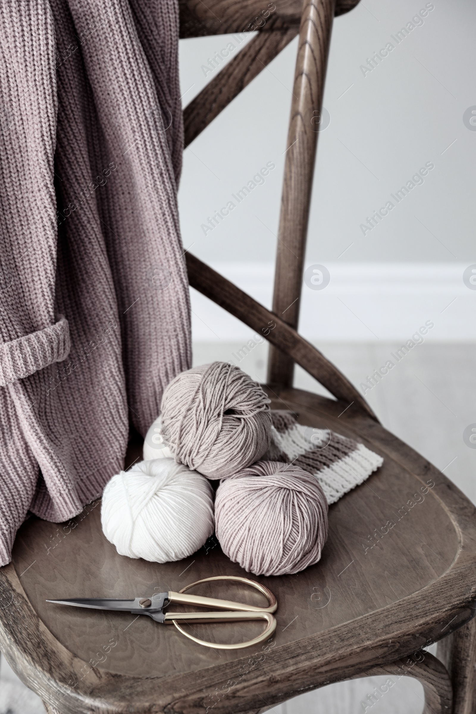 Photo of Yarn balls and scissors on wooden chair indoors. Creative hobby