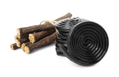 Tasty black candies and dried sticks of liquorice root on white background