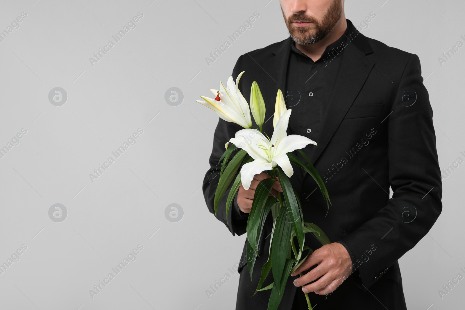 Photo of Man with white lilies on light grey background, closeup and space for text. Funeral ceremony