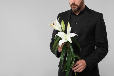 Man with white lilies on light grey background, closeup and space for text. Funeral ceremony