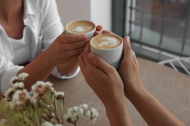 Photo of Friends drinking coffee at wooden table in cafe, closeup