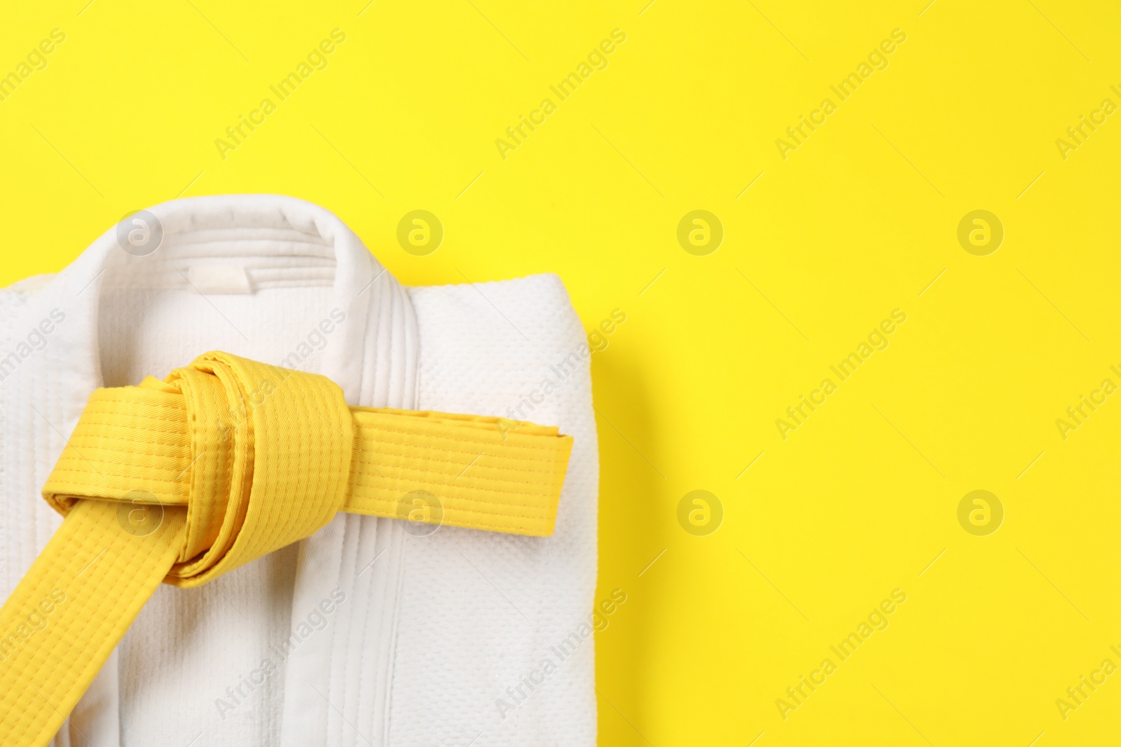 Photo of Karate belt and white kimono on yellow background, top view. Space for text