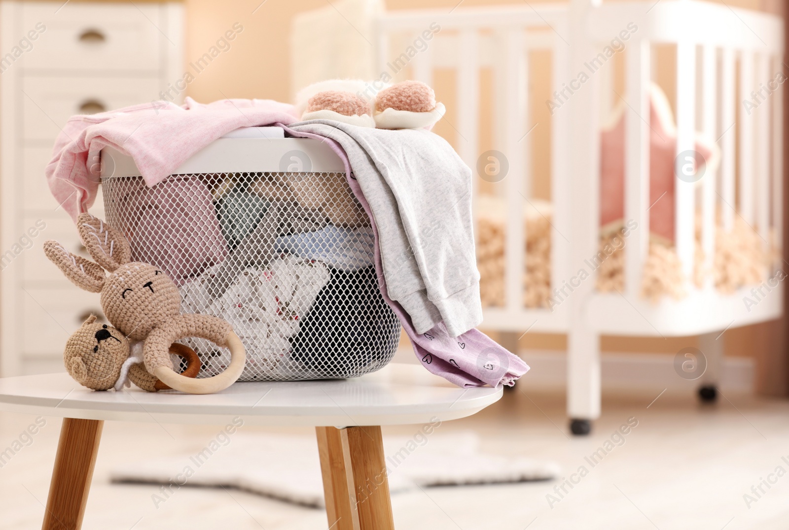 Photo of Laundry basket with baby clothes and crochet toys on white wooden table in child room, space for text