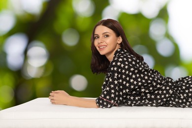 Image of Woman lying on comfortable mattress against blurred green background, bokeh effect. Sleep well - stay healthy