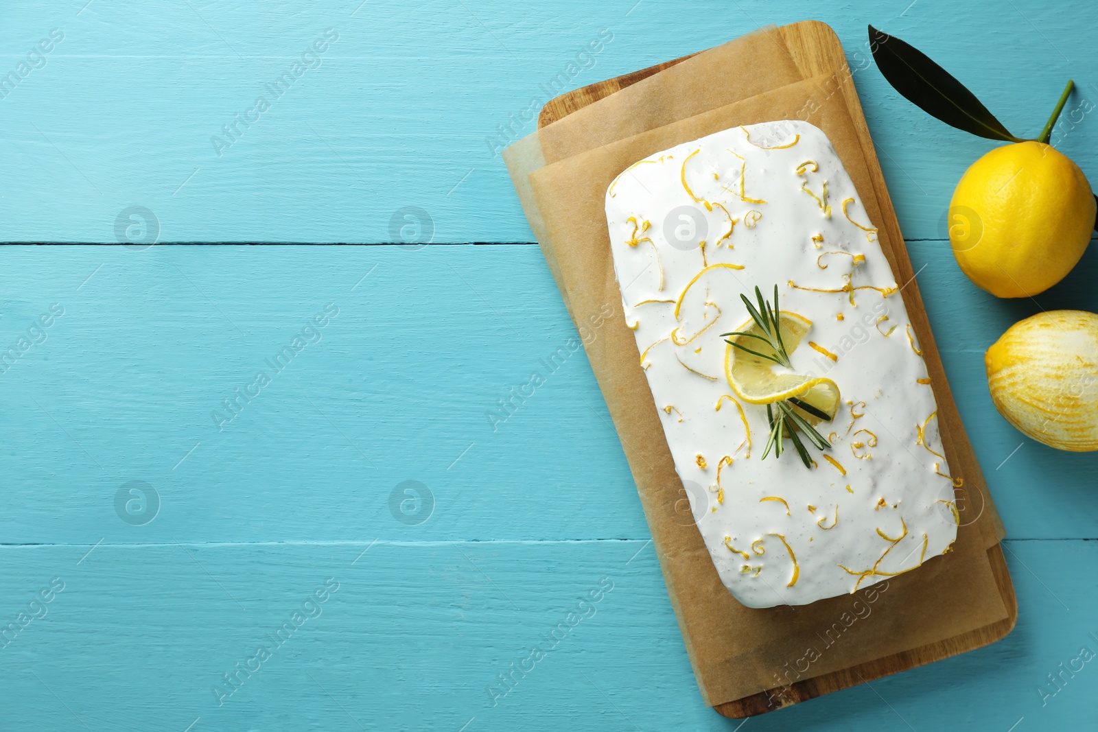 Photo of Tasty lemon cake with glaze and citrus fruits on light blue wooden table, flat lay. Space for text