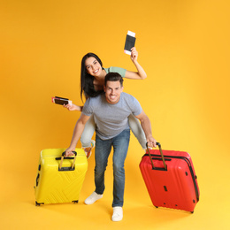 Photo of Happy couple with suitcases and passports for summer trip on yellow background. Vacation travel