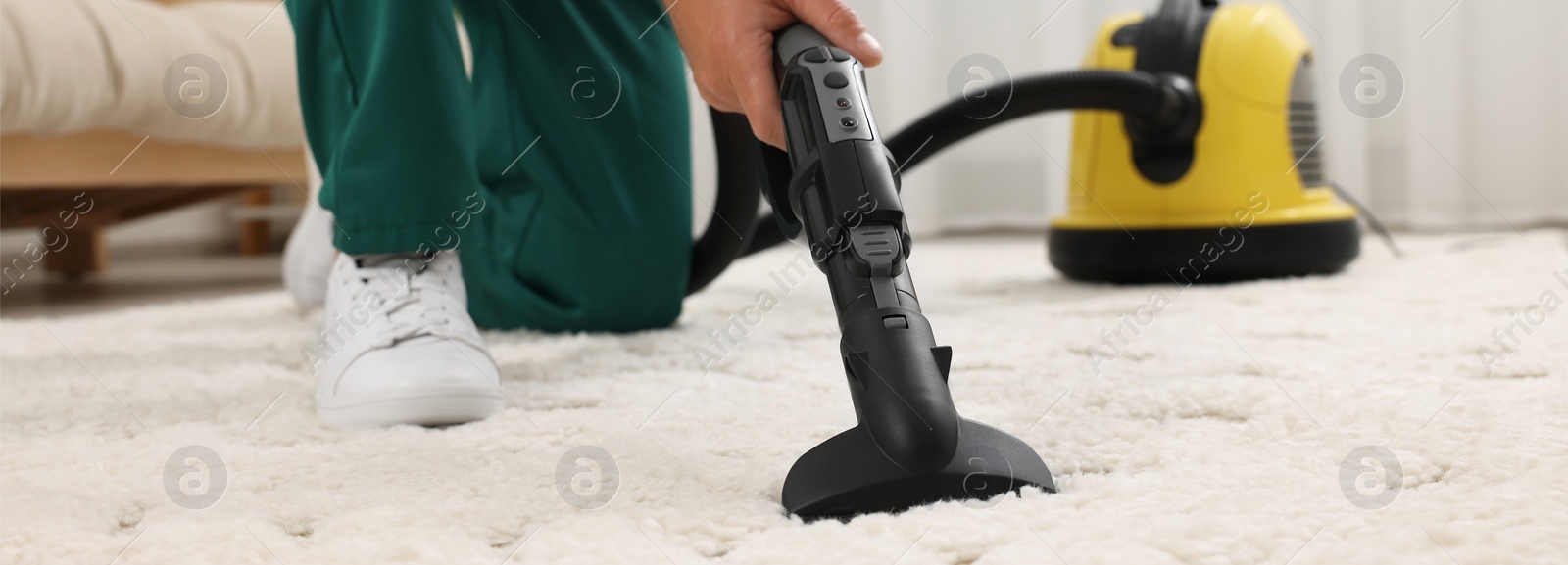 Image of Dry cleaner's employee hoovering carpet with vacuum cleaner in room, closeup. Banner design