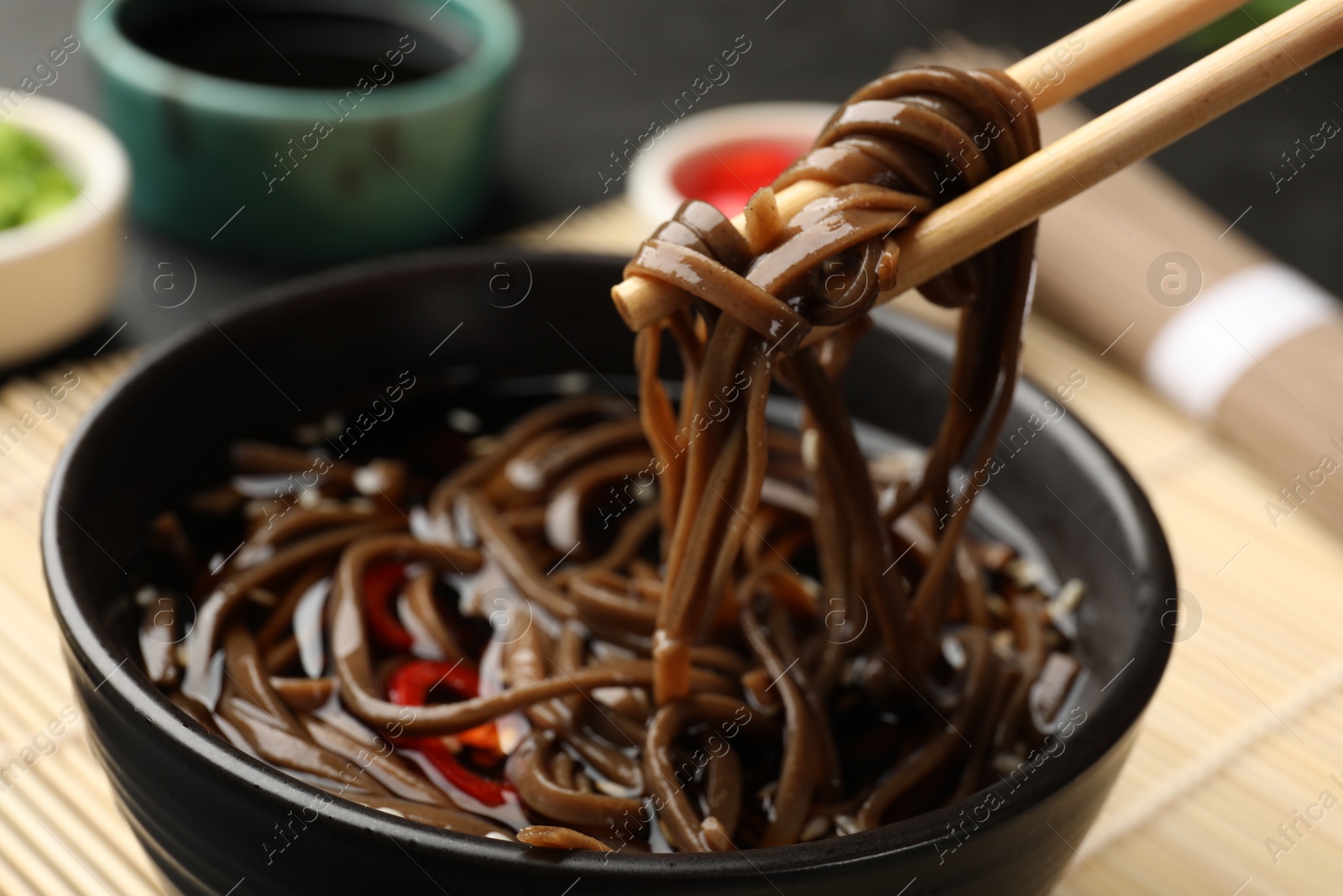 Photo of Eating delicious buckwheat noodle (soba) soup with chopsticks at table, closeup