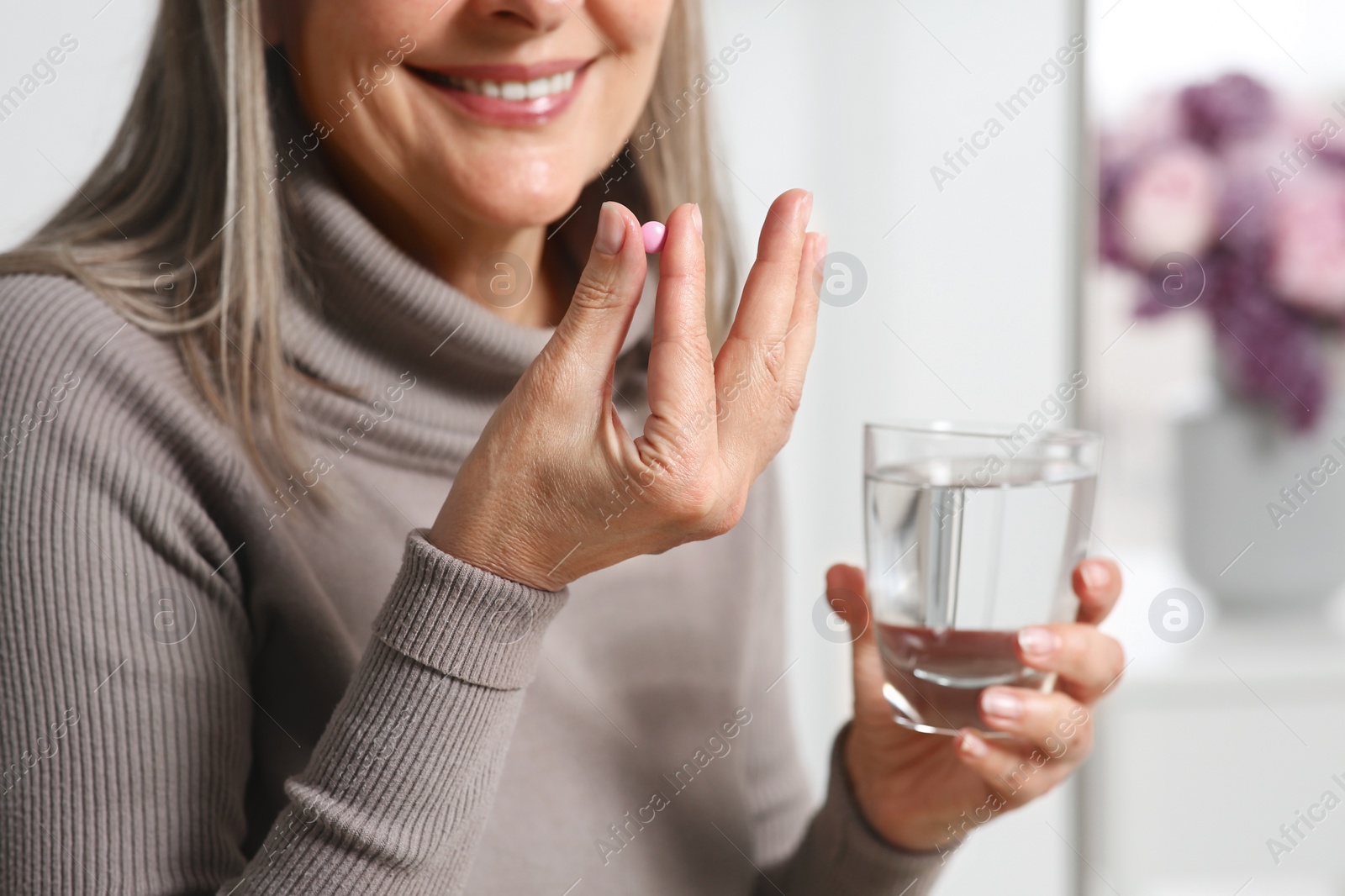 Photo of Senior woman with glass of water taking pill at home, closeup