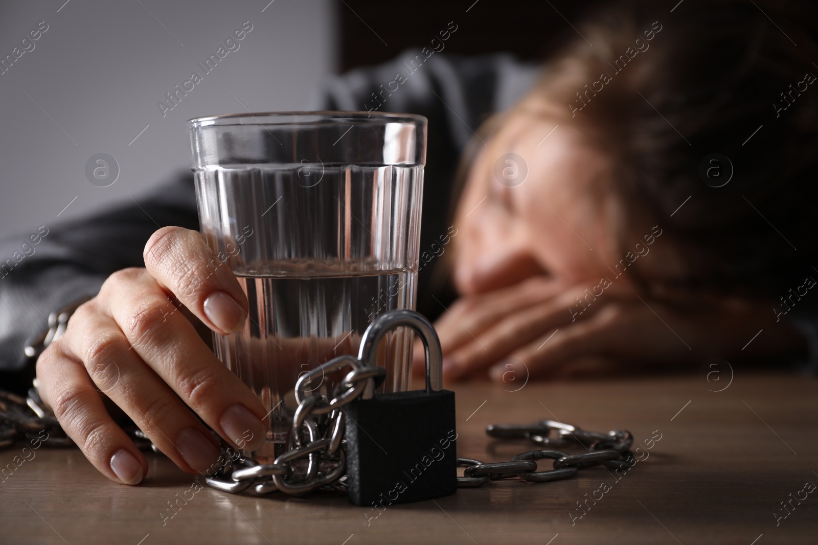 Photo of Alcohol addiction. Woman chained with glass of vodka sleeping on wooden table in room