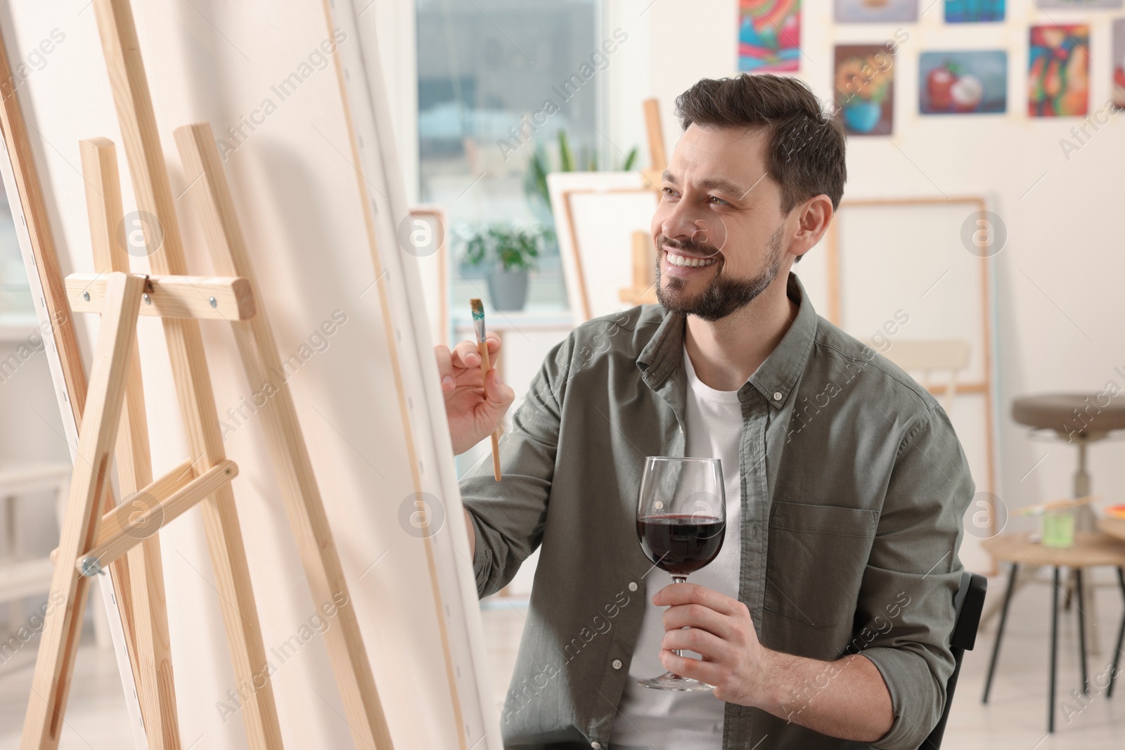 Photo of Handsome man with glass of wine painting in studio. Creative hobby