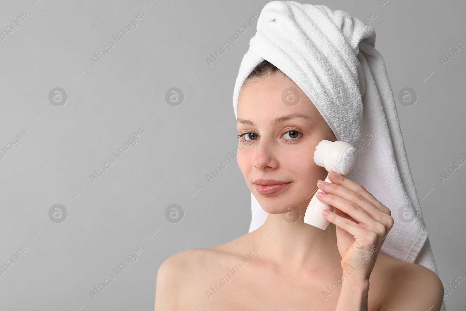 Photo of Washing face. Young woman with cleansing brush on grey background, space for text