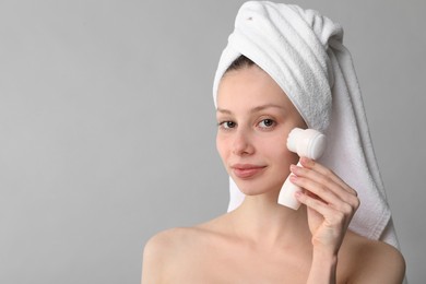 Washing face. Young woman with cleansing brush on grey background, space for text