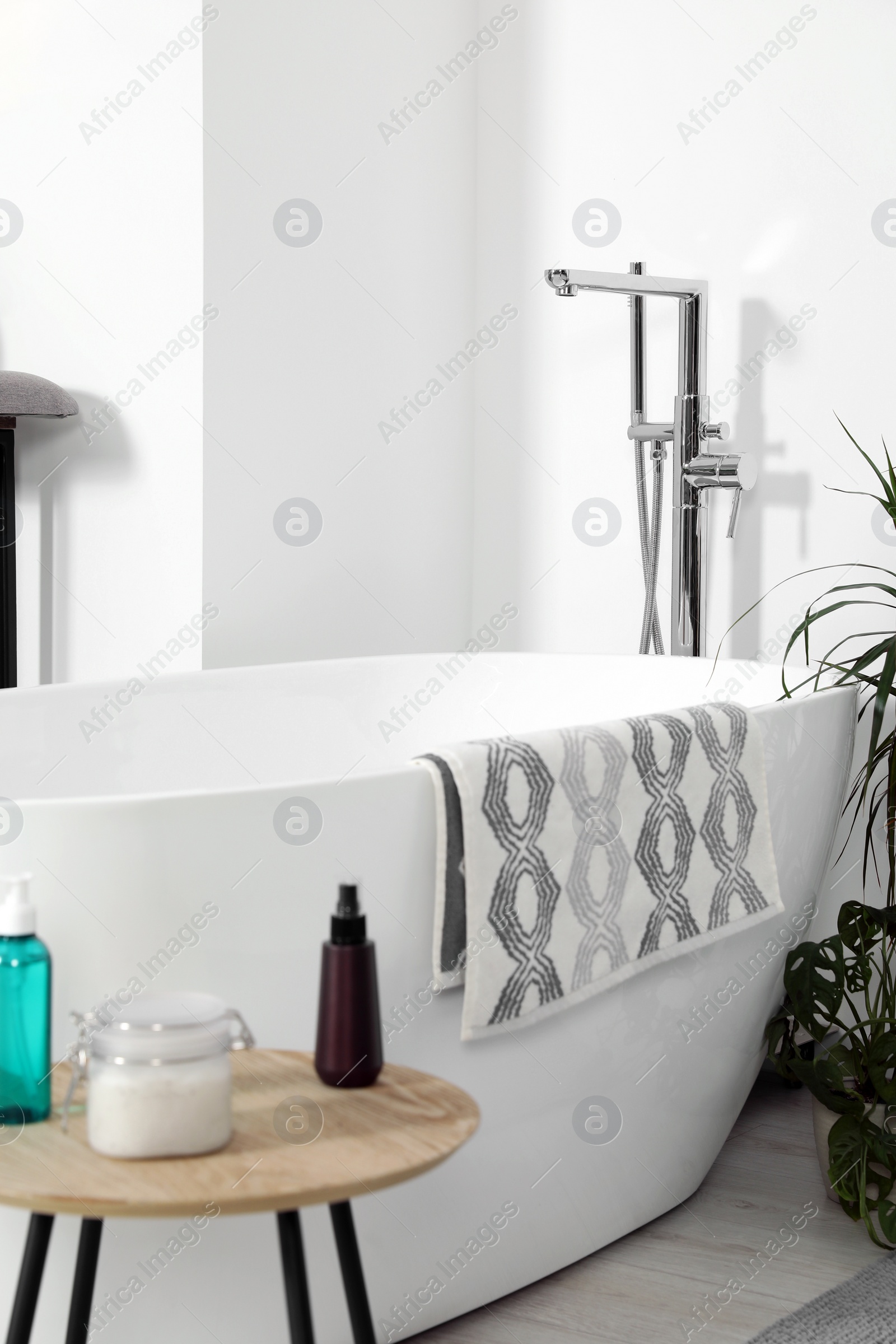 Photo of Stylish white tub and wooden table with toiletries in bathroom. Interior design