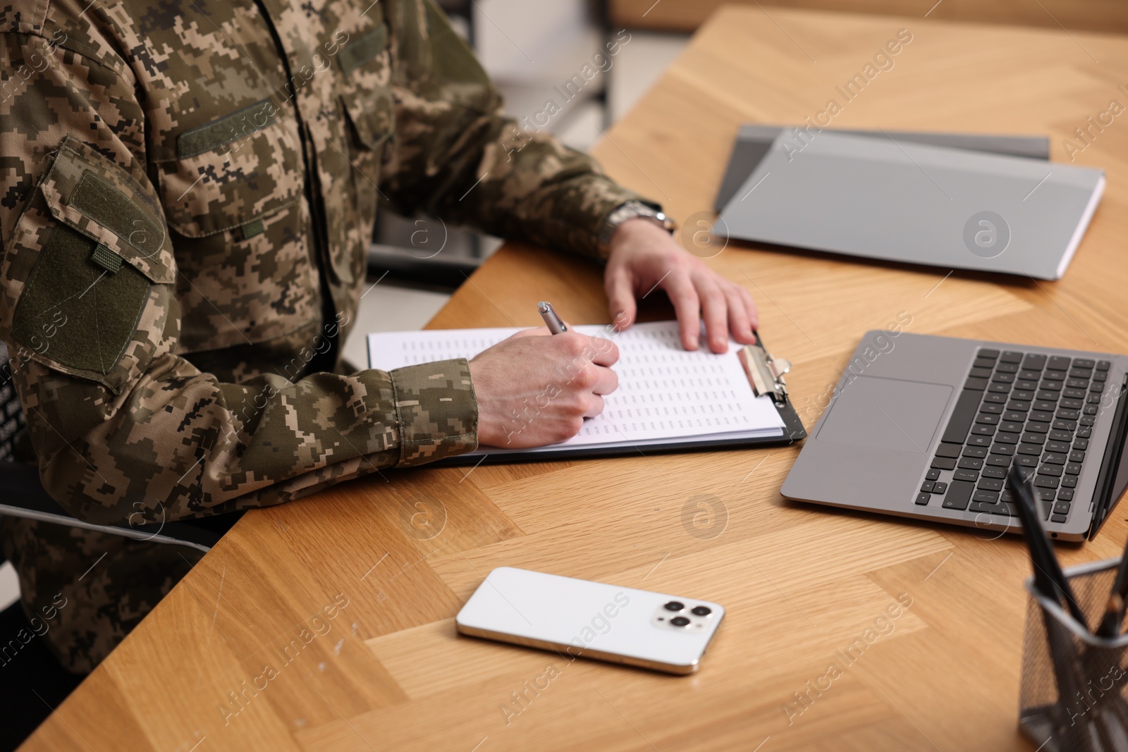 Photo of Military service. Soldier working at wooden table, closeup