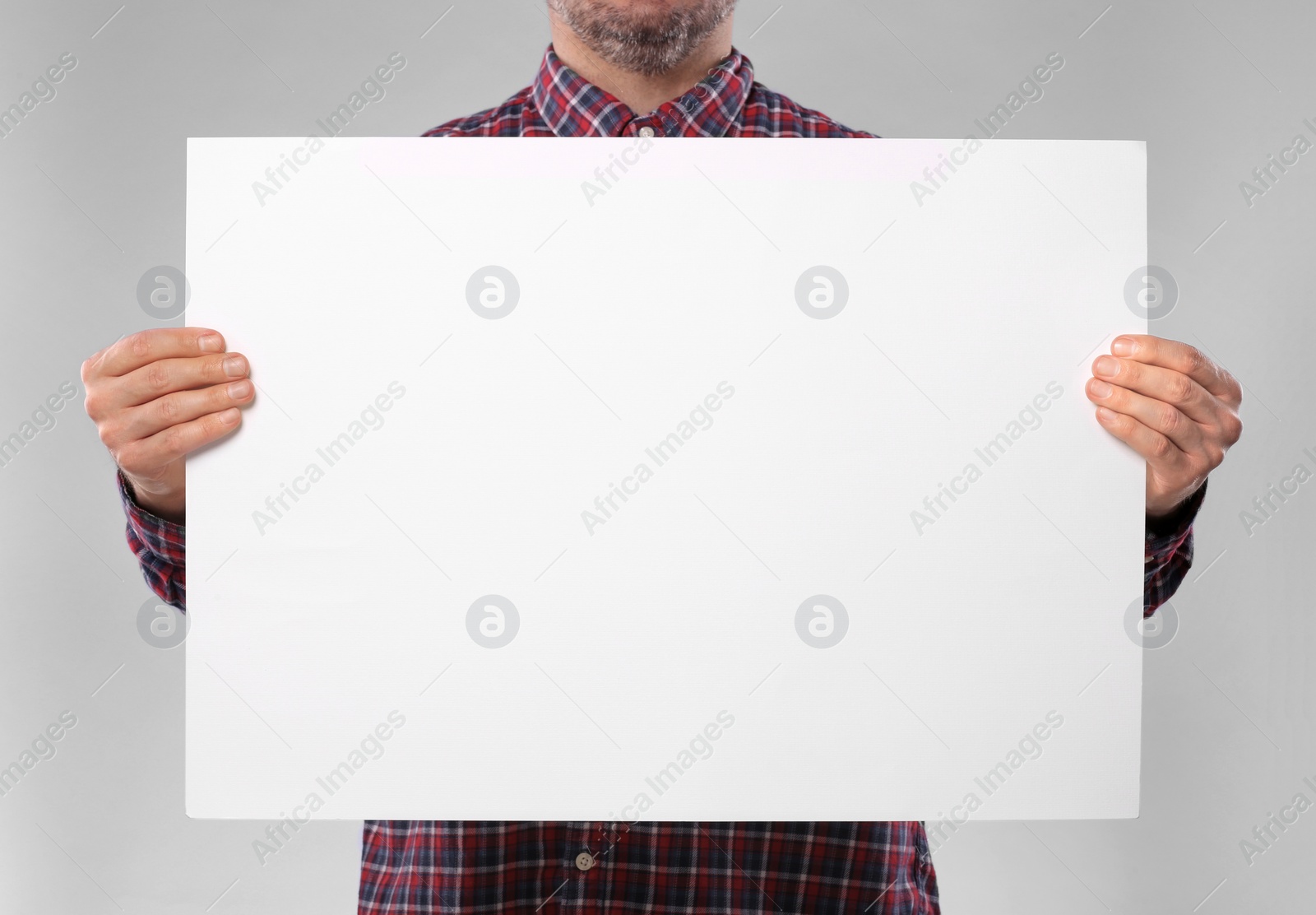 Photo of Man holding sheet of paper on grey background, closeup. Mockup for design