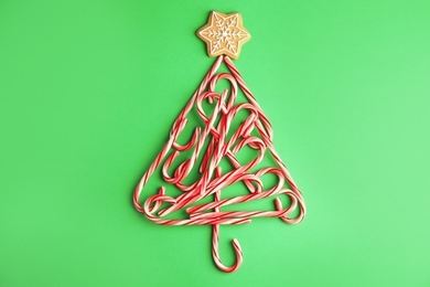 Photo of Christmas tree shape made with tasty candy canes on color background