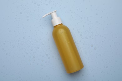 Photo of Wet bottle of face cleansing product on light blue background, top view