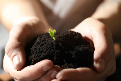 Photo of Woman holding soil with little green seedling, closeup