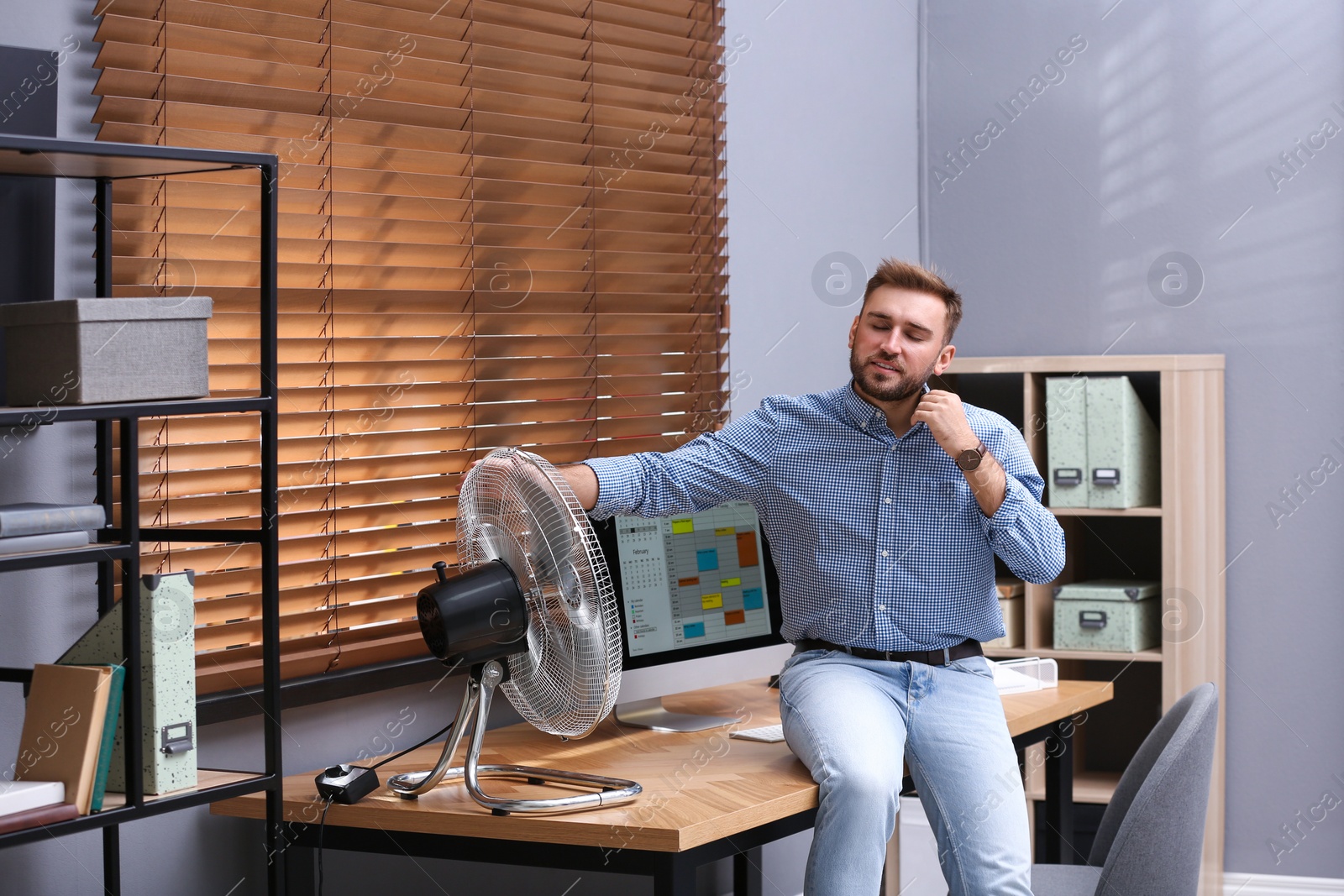 Photo of Man enjoying air flow from fan at workplace