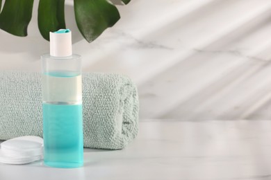 Photo of Bottle of micellar water, towel and cotton pads on white table against marble background, space for text