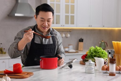Photo of Cooking process. Man tasting dish at countertop in kitchen