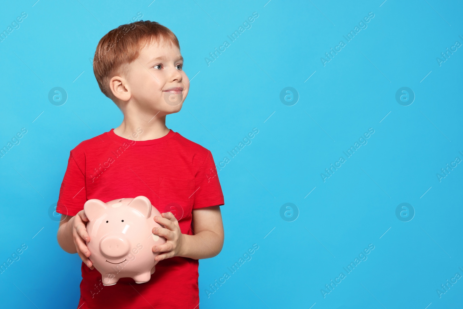 Photo of Cute little boy with ceramic piggy bank on light blue background, space for text