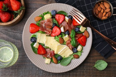 Photo of Tasty salad with brie cheese, prosciutto, almonds and berries served on wooden table, flat lay