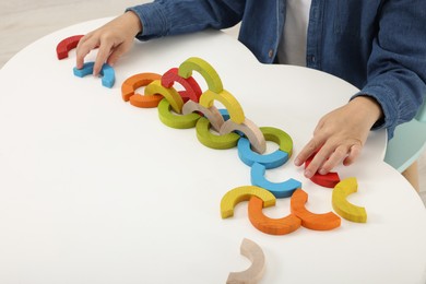 Photo of Motor skills development. Boy playing with colorful wooden arcs at white table, closeup