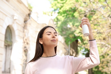 Young woman applying thermal water on face outdoors. Cosmetic product