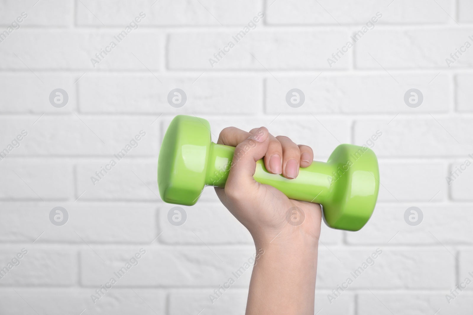 Photo of Woman holding dumbbell against brick wall, closeup. Home fitness