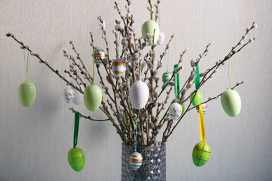 Beautiful willow branches with painted eggs in vase on light grey background. Easter decor