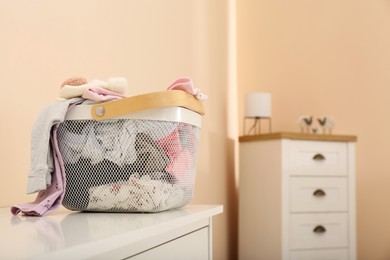 Photo of Laundry basket with baby clothes on white chest of drawers indoors, space for text