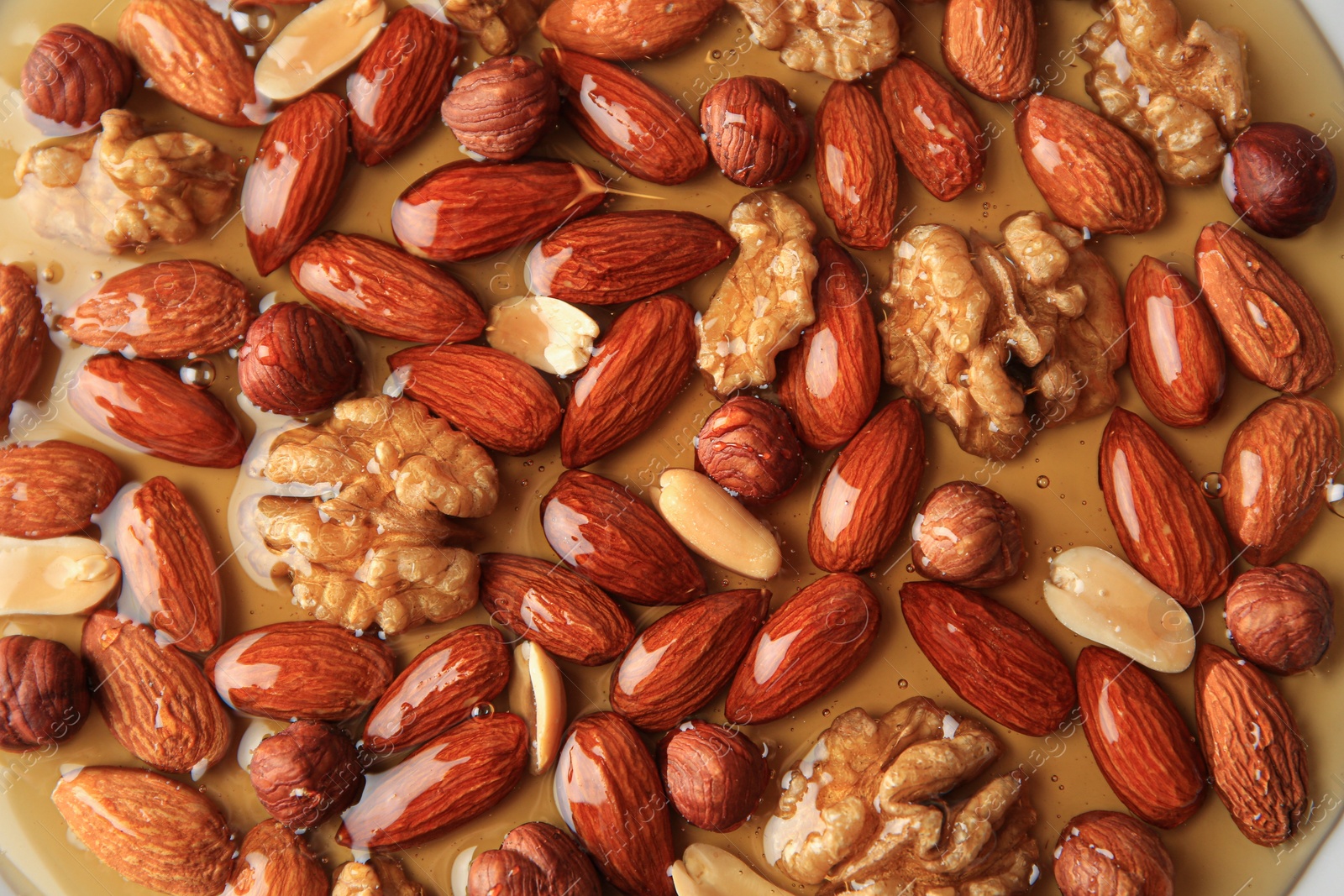 Photo of Different tasty nuts with honey as background, top view