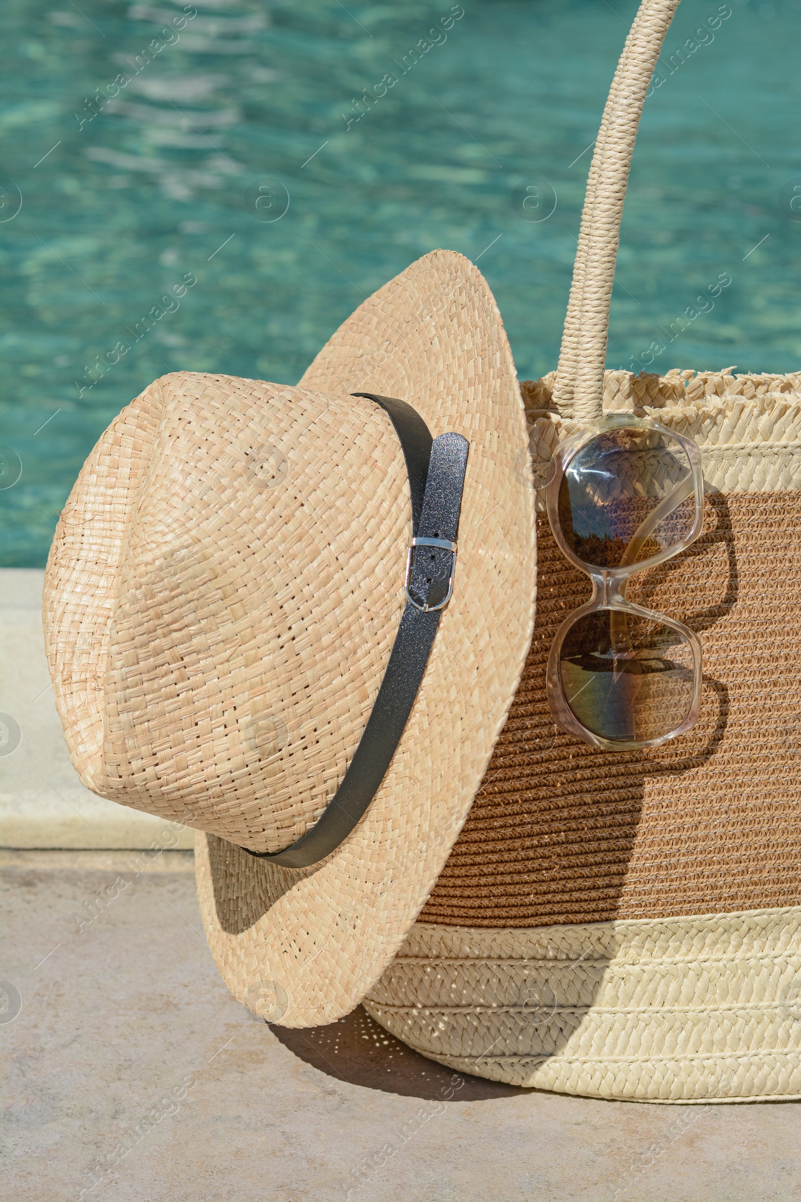 Photo of Stylish bag, sunglasses and hat near outdoor swimming pool on sunny day. Beach accessories