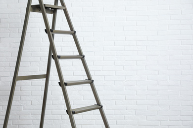 Photo of Metal stepladder near white brick wall. Space for text