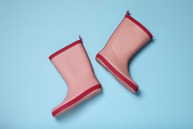 Photo of Pink rubber boots on light blue background, flat lay