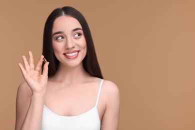 Photo of Beautiful young woman with vitamin pill on beige background. Space for text