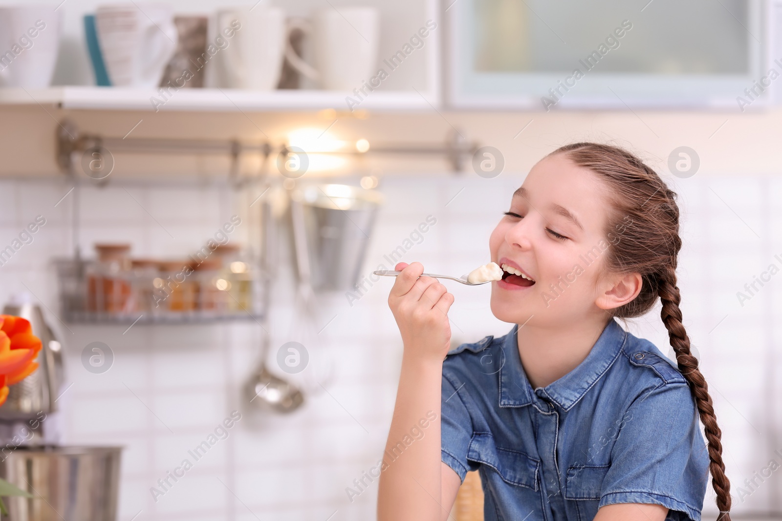 Photo of Cute girl eating tasty yogurt in kitchen